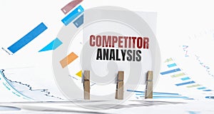 COMPETITOR ANALYSIS text on paper sheet with chart, dice, spectacles, pen, laptop and blue and yellow push pin on wooden table -