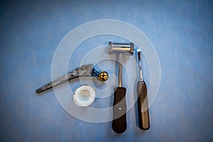 Complete explanted hip prosthesis lies next to a hammer and a chisel