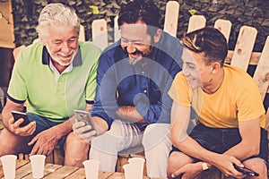 Complete family caucasian people men sitting on a wodd bench looking smartphones. grandfather father and son all together enjoying