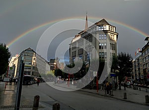 Complete rainbow surrounding a big building in a city corner