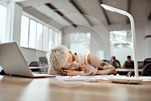 Completely exhausted. Young and tired tattooed business woman with short haircut sleeping at her workplace