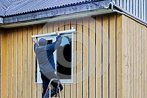 Completion of frame and panel house, roofer installs metal jambs on windows on outside.