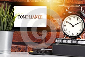 COMPLIANCE text with alarm clock, books and vase on brick background