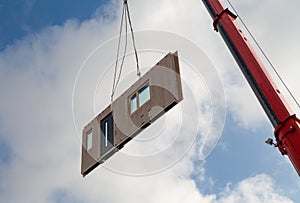 Component for a prefabricated house is transported from an orange jib of a mobile crane for assembly
