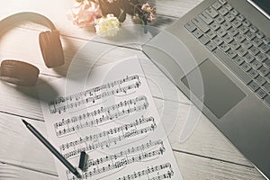 Compose music and education - paper sheet with musical notes, laptop and headphones on the artist desk