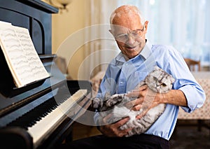 Composer with cat breed scottish fold in his arms sits next to piano