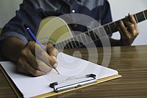 Composer holding pencil and writing lyrics in paper. Musician playing acoustic guitar