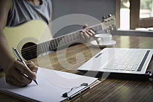 Composer holding pencil and writing lyrics in paper. Musician playing acoustic guitar