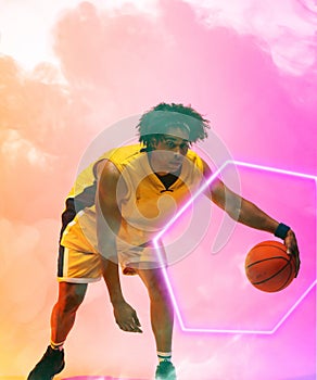 Composite of biracial basketball player dribbling ball by glowing hexagon on pink smoky background