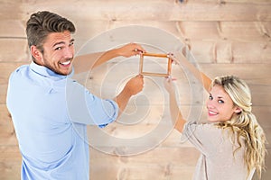 Composite image of attractive young couple hanging a frame