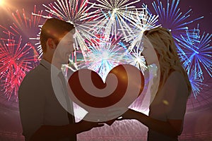 Composite image of attractive young couple holding red heart