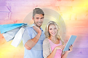 Composite image of attractive young couple holding shopping bags using tablet pc