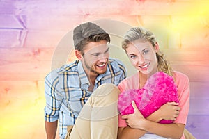 Composite image of attractive young couple sitting holding heart cushion