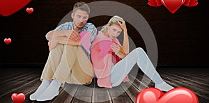 Composite image of attractive young couple sitting holding two halves of broken heart 3D