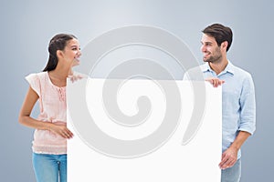 Composite image of attractive young couple smiling and holding poster