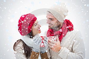 Composite image of attractive young couple in warm clothes holding mugs