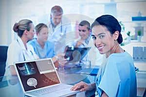 Composite image of beautiful smiling doctor typing on keyboard with her team behind