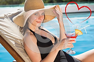 Composite image of beautiful woman holding drink by swimming pool