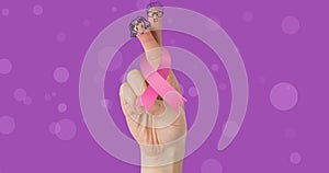 Composite image of breast cancer ribbon with hand gesture against purple background, copy space