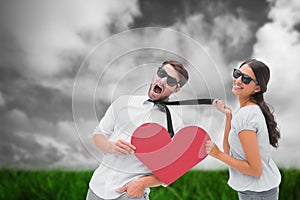 Composite image of brunette pulling her boyfriend by the tie holding heart