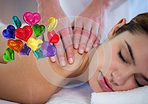Composite image of bunch of colorful heart shaped foil balloons against woman receiving a massage