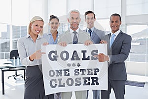 Composite image of business team holding large blank poster and pointing to it