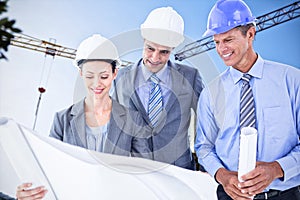 Composite image of businessmen and a woman with hard hats and holding blueprint