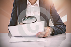 Composite image of businesswoman looking at document through magnifying glass