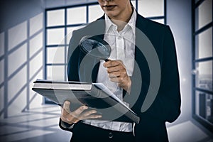 Composite image of businesswoman looking at document through magnifying glass