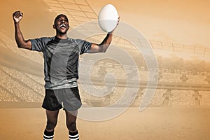 Composite image of cheerful sportsman with clenched fist holding rugby ball