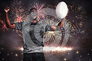 Composite image of cheerful sportsman with clenched fist holding rugby ball