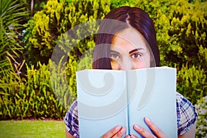 Composite image of close up portrait of woman hiding behind book