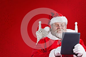 Composite image of close-up of santa claus holding digital tablet on armchair