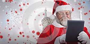 Composite image of close-up of santa claus holding digital tablet on armchair