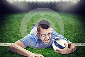 Composite image of confident rugby player lying in front with ball