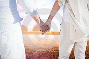 Composite image of couple on the beach looking out to sea holding hands