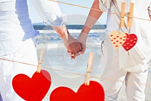 Composite image of couple on the beach looking out to sea holding hands