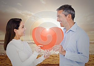 Composite image of couple holding red heart on beach