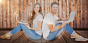 Composite image of couple sitting on floor back to back using laptop