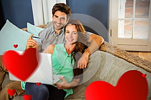 Composite image of couple on sofa and valentines hearts 3d