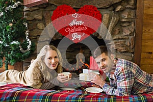 Composite image of couple with tea cups in front of lit fireplace