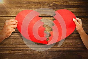 Composite image of cropped couple hands holding red cracked heart shape