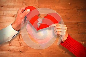 Composite image of cropped hands of couple holding cracked red heart shape