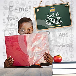 Composite image of cute boy reading book in library