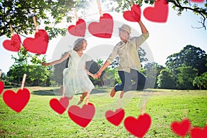 Composite image of cute couple jumping in the park together holding hands