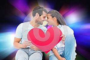 Composite image of cute couple sitting holding red heart