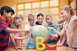 Composite image of cute pupils and teacher looking at globe in library