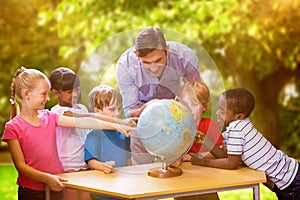 Composite image of cute pupils and teacher looking at globe in library