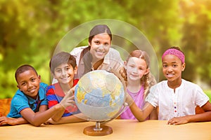 Composite image of cute pupils and teacher looking at globe in library