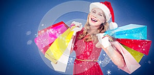 Composite image of excited blonde in santa hat holding shopping bags